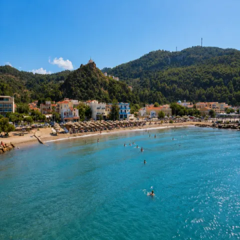 Karlovasi Port Beach in northwestern Samos with sand, small pebbles, clear blue water and organised umbrellas along the shore