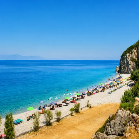 Tsampou Beach in Samos with large pebbles, deep blue sea and pine trees around the bay